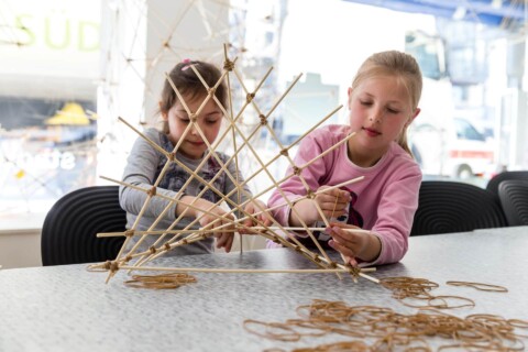 Bambini bauen mit Strohhalmen eine kreative Struktur am Tisch im Museum.