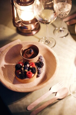 Ein Dessert mit Beeren und Schokolade auf einem Tisch bei Kerzenlicht.