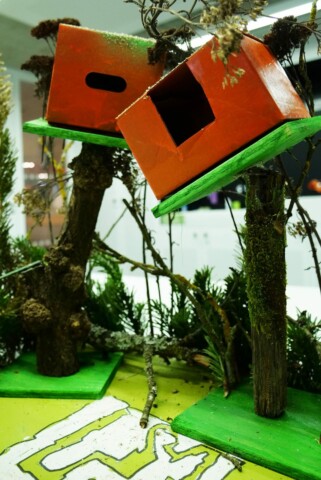 Kunstinstallation mit bunten, schräg stehenden Holzkästen in einem urbanen Garten.