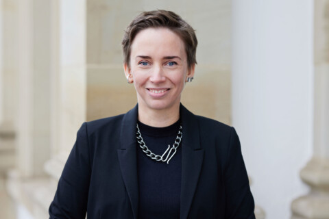 Ein professionelles Porträt einer Frau im Business-Outfit vor einer historischen Kulisse, Team.