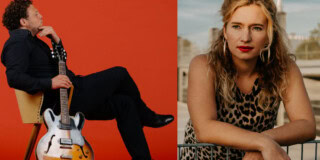 Ein Duo-Musiker mit Gitarre und eine Frau mit lockigem Haar vor urbaner Kulisse, k.