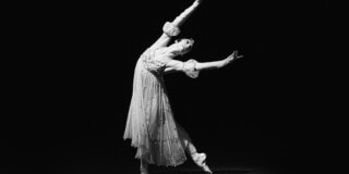 Eine Balletttänzerin in einer eleganten Pose auf der Bühne, schwarz-weiße Aufnahme.