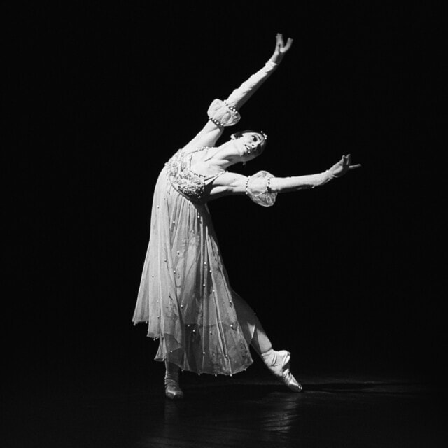 Elegante Balletttänzerin in weißem Kostüm auf schwarzem Hintergrund.