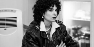 Eindrucksvolle Frau mit lockigem Haar in schwarzer Lederjacke im Museum, k.
