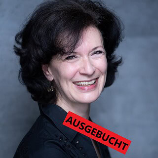 Eine lachende Frau mit dunklem Haar, auf einem grauen Hintergrund, mit rotem 