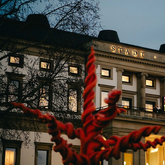 Der StadtPalais Stuttgart bei Nacht mit beleuchteter Fassade und Skulptur im Vordergrund.