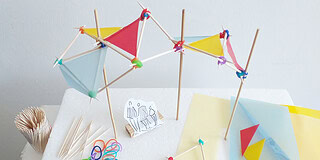 Bunte Sonnenschirme aus Papier und Holzstäbchen, Bastelmaterialien auf Styroporplatte.
