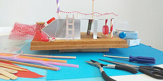 Kreatives DIY-Miniaturmodell mit bunten Materialien und Werkzeugen auf blauer Unterlage.
