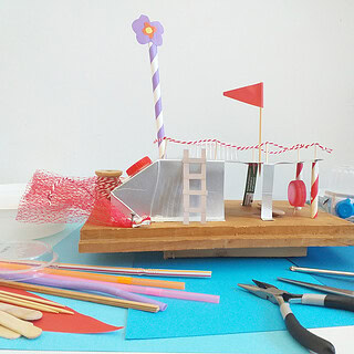 Kreatives DIY-Miniaturmodell mit bunten Materialien und Werkzeugen auf blauer Unterlage.