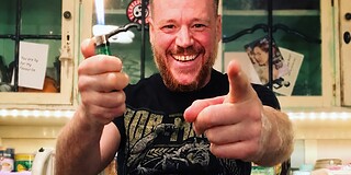 Fröhlicher Mann mit Feuerzeug in Küche, lächelnd und zeigend.