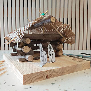 Handgefertigtes Blockhaus-Modell aus Holz mit Werkzeugen im Hintergrund.