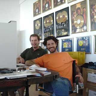 Zwei Männer im Musikstudio vor Goldplatten an der Wand.